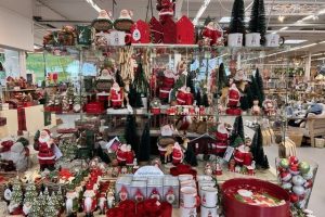 Regal mit vielfältigen Weihnachtsdekorationen wie Weihnachtsmännern, Tannenbäumen, Kerzenhaltern, Tassen und Schalen in einem Geschäft.