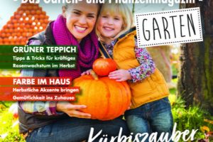 Frau und Kind halten großen orangefarbenen Kürbis im Garten, umgeben von Herbstlaub und weiteren Kürbissen.