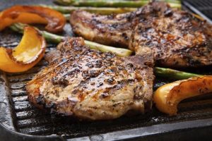 Gegrillte Schweinekoteletts mit Gewürzen und gebratenem Kürbis auf Grillpfanne.